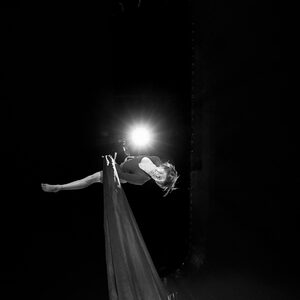Un artiste éclairé par un projecteur unique, un drap blanc déployé autour de lui.