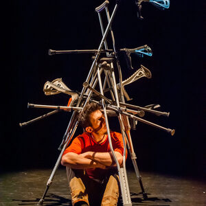 Un artiste assis en fauteuil roulant devant la structure de béquilles.