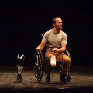Un artiste amputé assis dans son fauteuil roulant, la prothèse posée au sol.